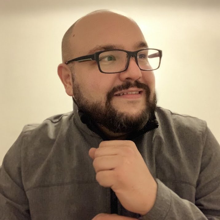 Portrait of a man with glasses and a beard, wearing a gray jacket, smiling and looking towards the side.